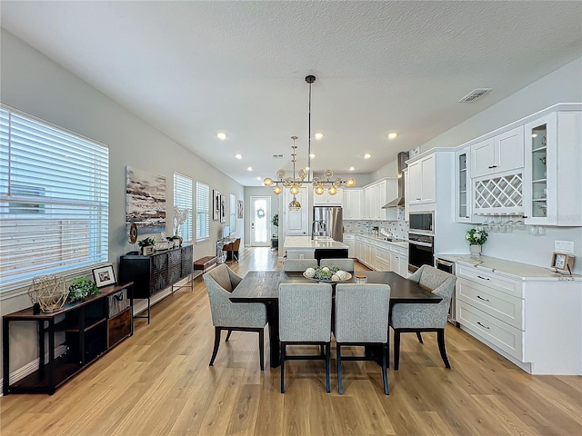 dining space featuring light hardwood / wood-style floors, a textured ceiling, and a notable chandelier