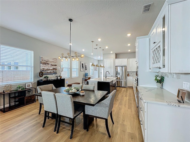 dining room with sink, a textured ceiling, a chandelier, and light hardwood / wood-style flooring