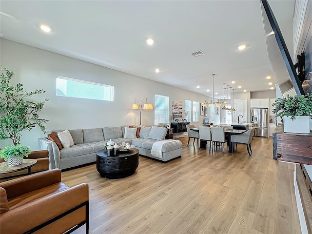 living room featuring an inviting chandelier, sink, and light hardwood / wood-style flooring