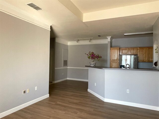 kitchen featuring crown molding, dark wood-type flooring, stainless steel fridge, track lighting, and kitchen peninsula