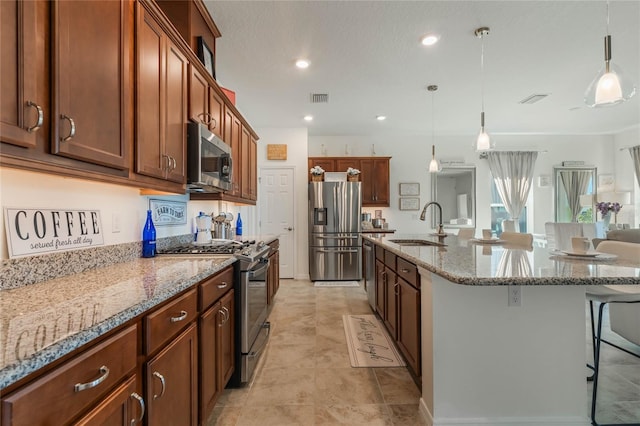 kitchen with sink, a breakfast bar, appliances with stainless steel finishes, hanging light fixtures, and a large island with sink