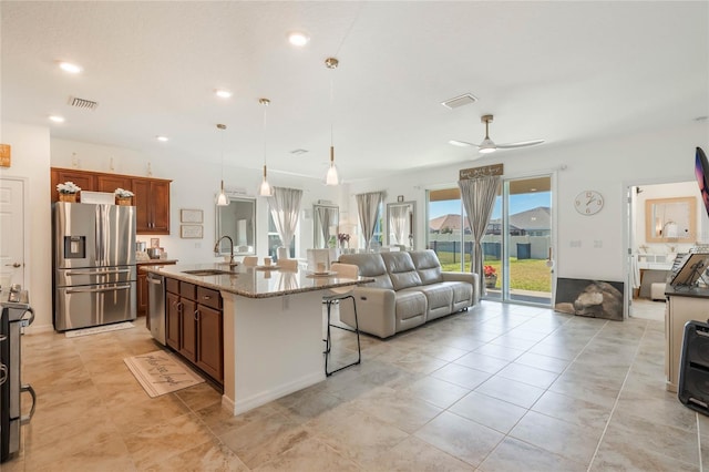 kitchen with pendant lighting, sink, stainless steel appliances, light stone counters, and an island with sink