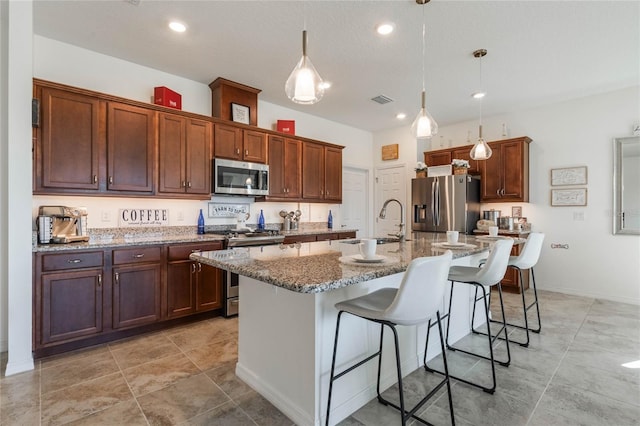 kitchen with pendant lighting, sink, a breakfast bar area, stainless steel appliances, and a center island with sink