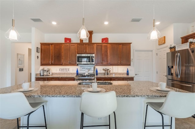 kitchen with decorative light fixtures, a center island with sink, a breakfast bar area, and appliances with stainless steel finishes