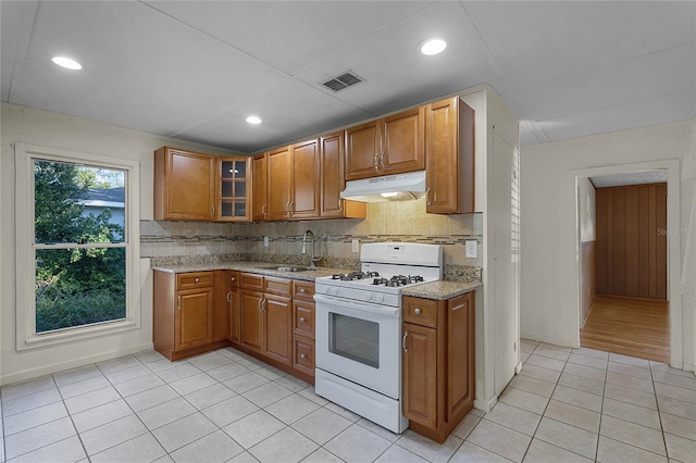 kitchen with sink, light tile patterned floors, backsplash, light stone counters, and white gas stove