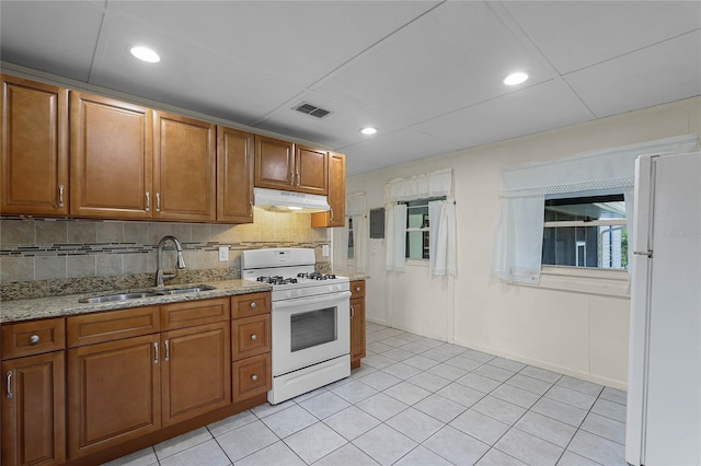 kitchen featuring sink, white appliances, light tile patterned floors, backsplash, and light stone countertops