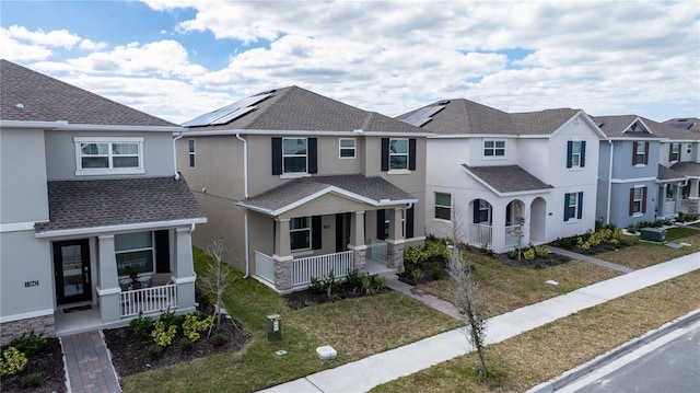 townhome / multi-family property with a porch, a front yard, and solar panels