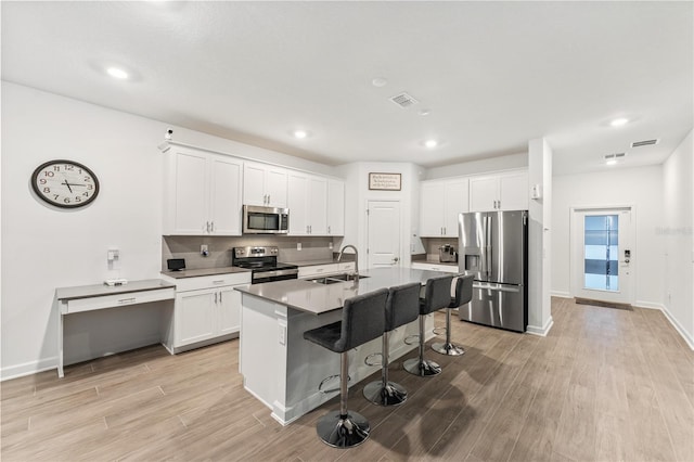 kitchen featuring sink, appliances with stainless steel finishes, white cabinetry, a kitchen breakfast bar, and a center island with sink