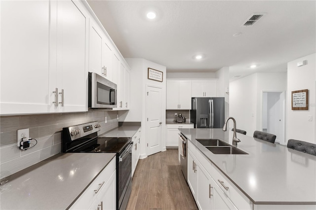 kitchen with white cabinetry, an island with sink, sink, stainless steel appliances, and dark wood-type flooring