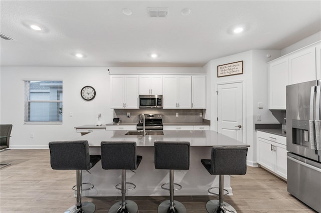 kitchen with sink, white cabinetry, a center island with sink, stainless steel appliances, and light hardwood / wood-style floors