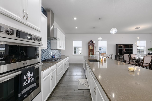 kitchen with appliances with stainless steel finishes, white cabinetry, sink, dark stone countertops, and wall chimney exhaust hood