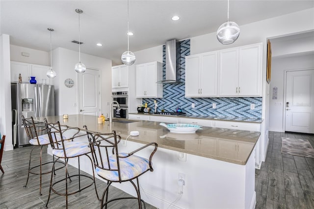 kitchen with stainless steel appliances, a kitchen breakfast bar, light stone counters, a center island with sink, and wall chimney exhaust hood