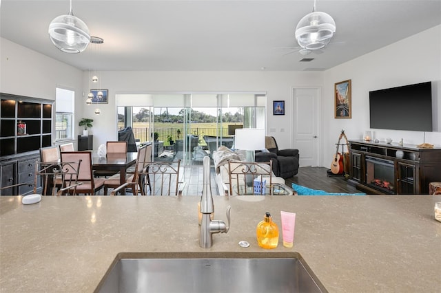 kitchen featuring pendant lighting, ceiling fan, a fireplace, and sink