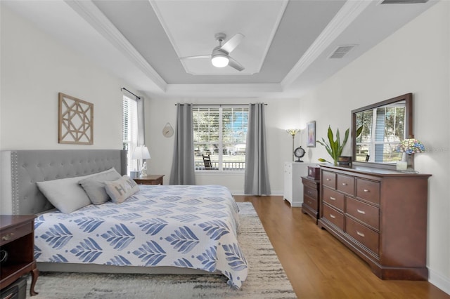 bedroom with a raised ceiling, wood-type flooring, ceiling fan, and crown molding