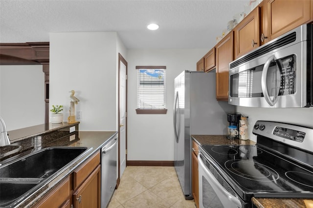 kitchen with appliances with stainless steel finishes, sink, dark stone counters, and light tile patterned floors