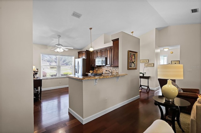 kitchen with lofted ceiling, appliances with stainless steel finishes, kitchen peninsula, a wealth of natural light, and light stone countertops