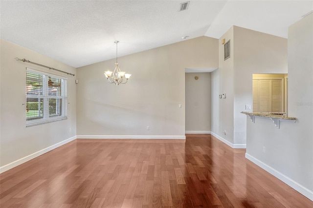 unfurnished dining area with visible vents, baseboards, light wood finished floors, a notable chandelier, and vaulted ceiling