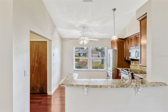 kitchen featuring a kitchen breakfast bar, brown cabinetry, dark wood finished floors, a peninsula, and stainless steel appliances