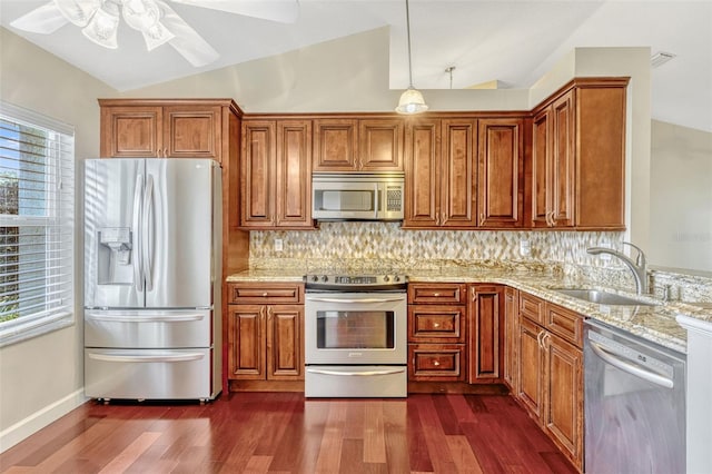 kitchen with brown cabinets, a sink, stainless steel appliances, a ceiling fan, and vaulted ceiling
