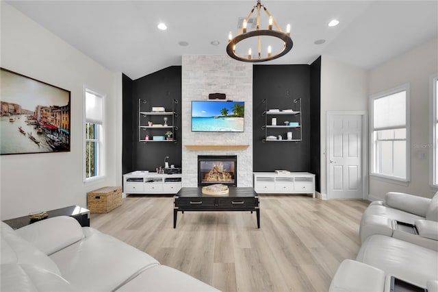 living room with vaulted ceiling, an inviting chandelier, a fireplace, and light hardwood / wood-style floors