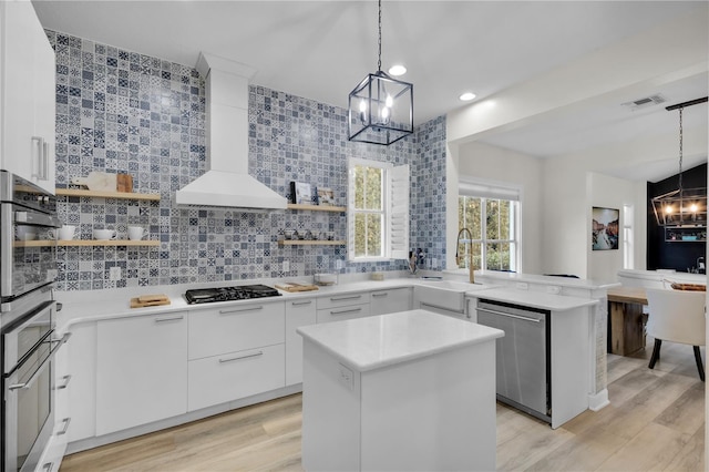 kitchen featuring wall chimney exhaust hood, hanging light fixtures, gas cooktop, dishwasher, and white cabinets