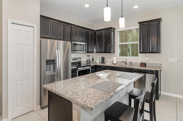 kitchen with pendant lighting, light tile patterned floors, sink, appliances with stainless steel finishes, and a kitchen island