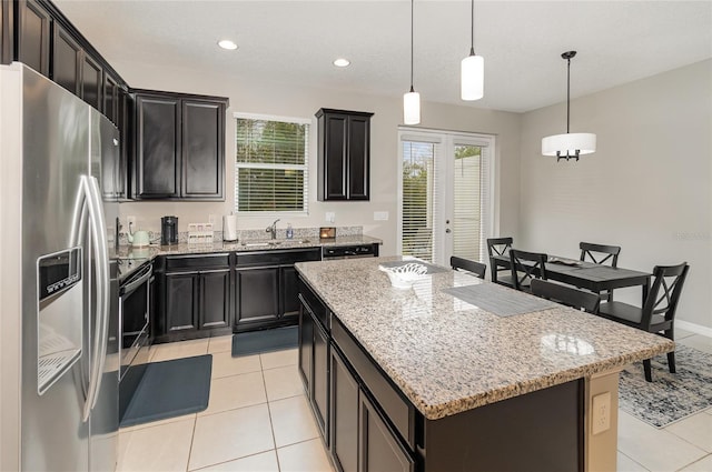 kitchen featuring stainless steel refrigerator with ice dispenser, sink, light stone counters, decorative light fixtures, and a kitchen island