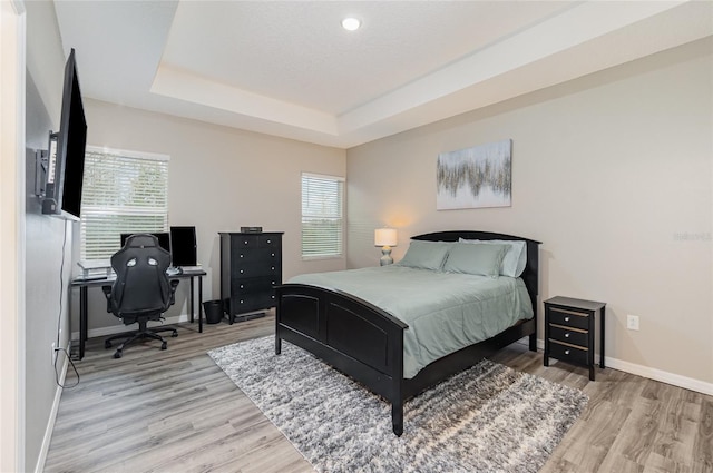 bedroom featuring multiple windows, light wood-type flooring, and a tray ceiling