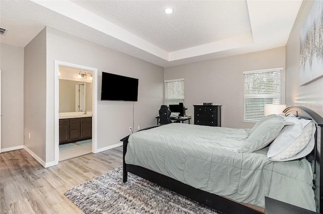 bedroom with light hardwood / wood-style flooring, a raised ceiling, a textured ceiling, and ensuite bathroom