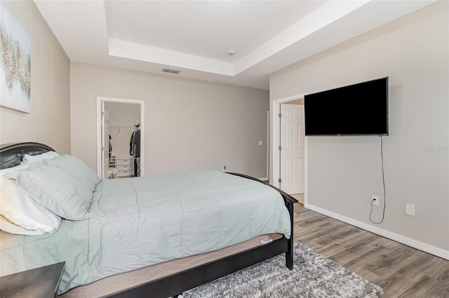 bedroom featuring a closet, a spacious closet, hardwood / wood-style floors, and a raised ceiling