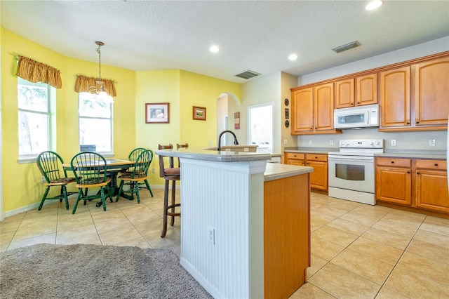 kitchen with white appliances, light tile patterned floors, visible vents, arched walkways, and an island with sink