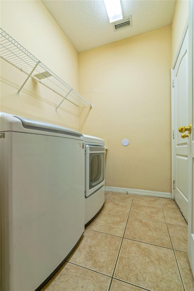 clothes washing area with laundry area, baseboards, independent washer and dryer, a textured ceiling, and light tile patterned flooring