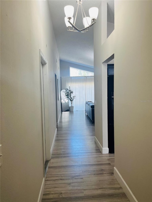 corridor featuring wood-type flooring, lofted ceiling, and an inviting chandelier