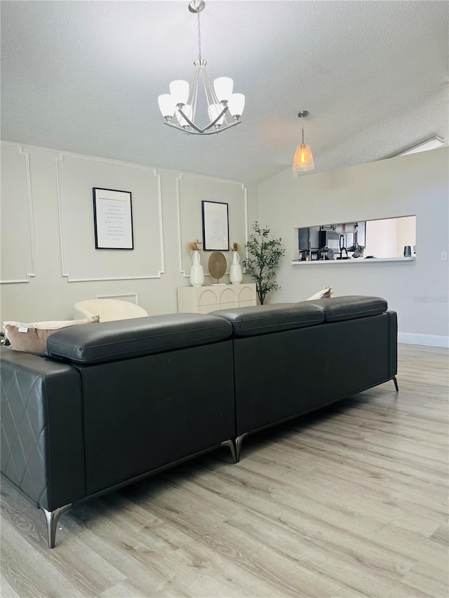 living room with an inviting chandelier, a textured ceiling, and light hardwood / wood-style flooring