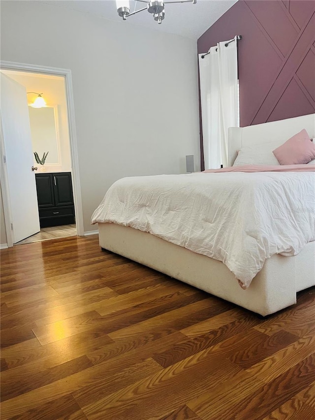 bedroom featuring hardwood / wood-style flooring, connected bathroom, and an inviting chandelier