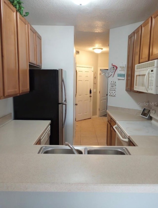 kitchen featuring white appliances, sink, a textured ceiling, and light tile patterned floors