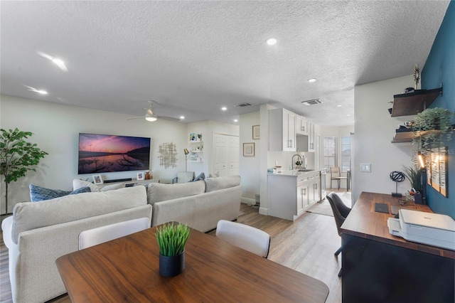 dining area with ceiling fan, sink, a textured ceiling, and light wood-type flooring