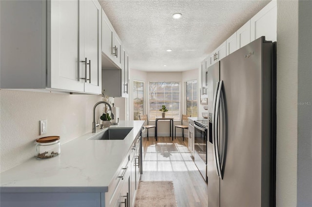 kitchen featuring range with electric stovetop, sink, white cabinets, stainless steel fridge with ice dispenser, and light stone countertops