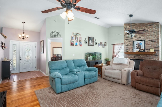 living room with a brick fireplace, a chandelier, vaulted ceiling, and light hardwood / wood-style flooring