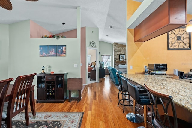 dining space with ceiling fan, lofted ceiling, a textured ceiling, and light hardwood / wood-style floors