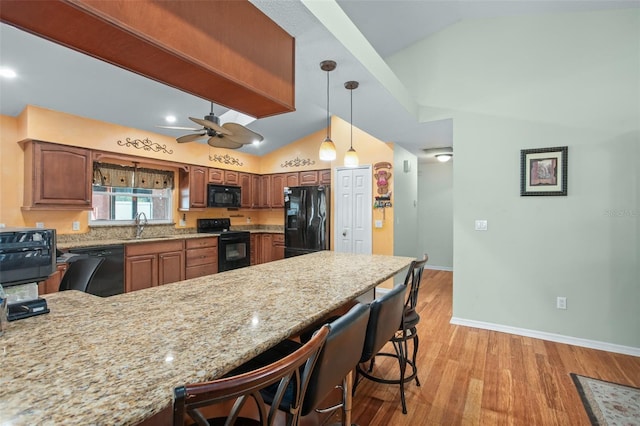 kitchen featuring sink, vaulted ceiling, hanging light fixtures, a kitchen breakfast bar, and black appliances