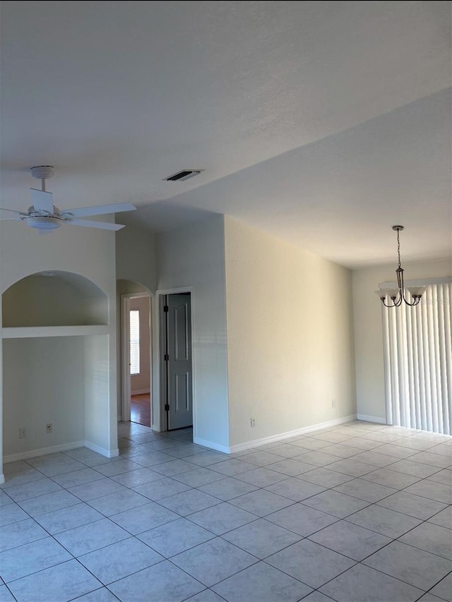 tiled spare room featuring ceiling fan with notable chandelier