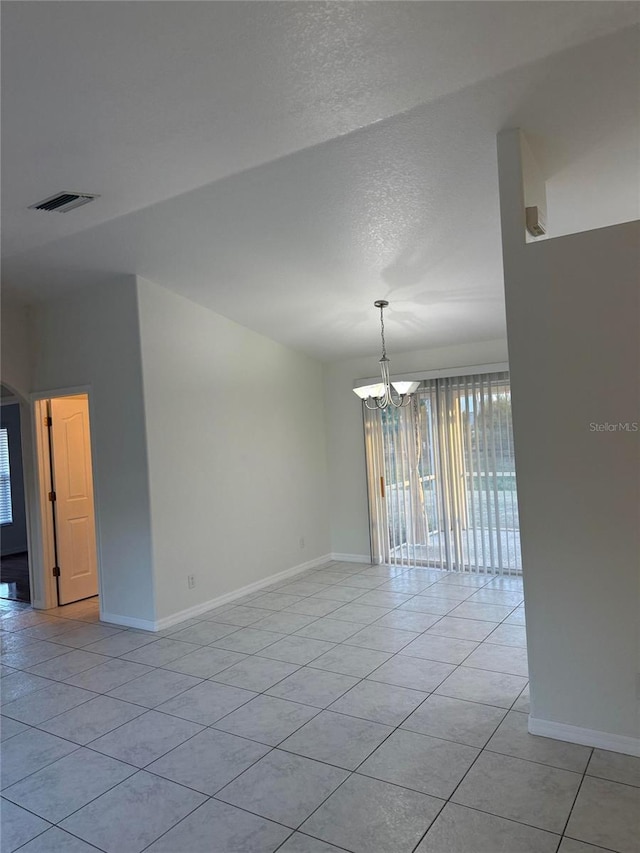 tiled empty room featuring a textured ceiling and an inviting chandelier