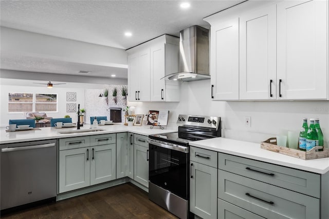 kitchen with sink, appliances with stainless steel finishes, a textured ceiling, kitchen peninsula, and wall chimney exhaust hood