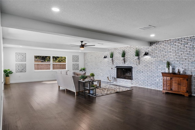 living room with ceiling fan, a textured ceiling, brick wall, dark hardwood / wood-style flooring, and a brick fireplace