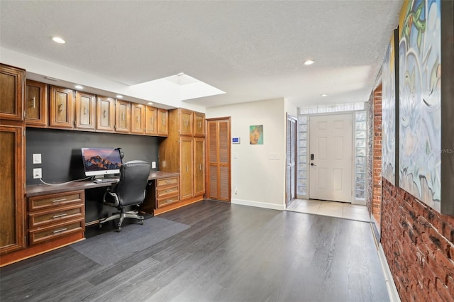 office space featuring a skylight, built in desk, wood-type flooring, a textured ceiling, and brick wall