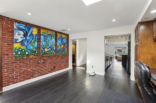 hall with dark wood-type flooring, brick wall, and a textured ceiling