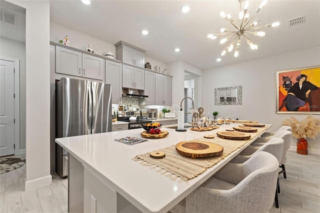 kitchen with stainless steel fridge, a kitchen breakfast bar, an island with sink, and gray cabinets