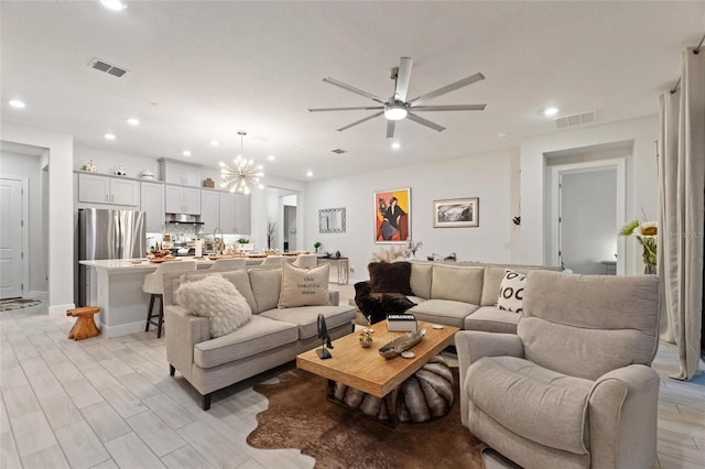 living room featuring ceiling fan with notable chandelier and light wood-type flooring