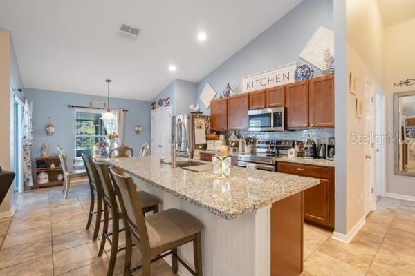 kitchen with lofted ceiling, decorative light fixtures, stainless steel appliances, and a center island with sink